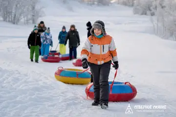 Инструктор ведет гостей с тюбингами по снегу